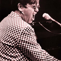 Elton John auf der Bühne am Klavier in kariertem Jackett